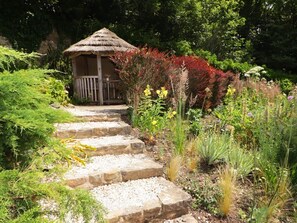 A garden pathway leading to a wooden gazebo with a thatched roof.