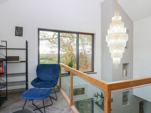 Ein modernes Zimmer mit blauem Sessel, großem Fenster, einer Kristallleuchtre und einer Glastrennwand.