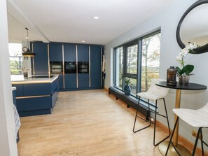 A modern kitchen with blue cabinetry, a large window, and a dining area with a round table and two chairs.