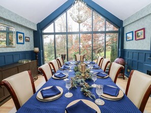 A dining room with a long table set for six, blue walls, and large windows.