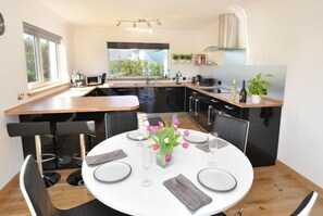 Une cuisine moderne avec un coin repas, de grandes fen êtres et une vue sur la verdure.