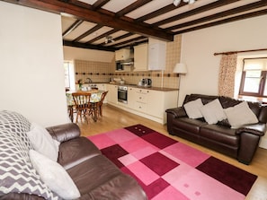 Una sala de estar con un sofá de cuero marrón, un sofá estampado, una cocina con salpicadero de azulejos y un comedor con mesa y sillas.