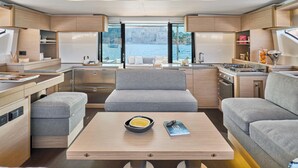 A compact, modern interior with a kitchenette, seating area, and large windows offering a view of the water. - Sun-Kissed Sailing Adventure in Islas Sarónicas (Alimos)