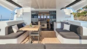 A yacht interior with a dining area, two sofas, a table, and a kitchen. - Sun-Kissed Sailing Adventure in Islas Sarónicas (Alimos)