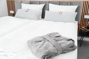 Habitación de hotel con una cama doble, dos mesitas de noche, cabecera gris y una bata gris sobre la cama.