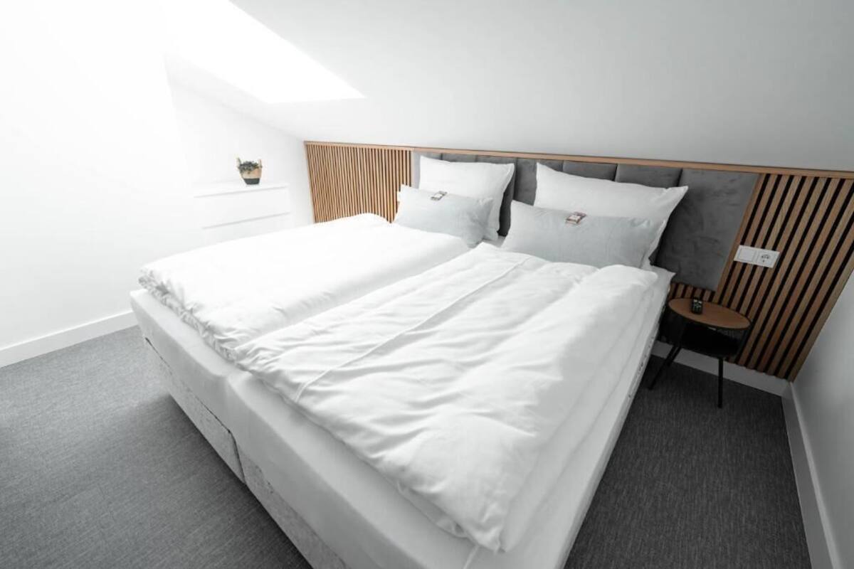 Habitación de hotel moderna con una cama grande, una mesita de noche pequeña y vista al cielo.