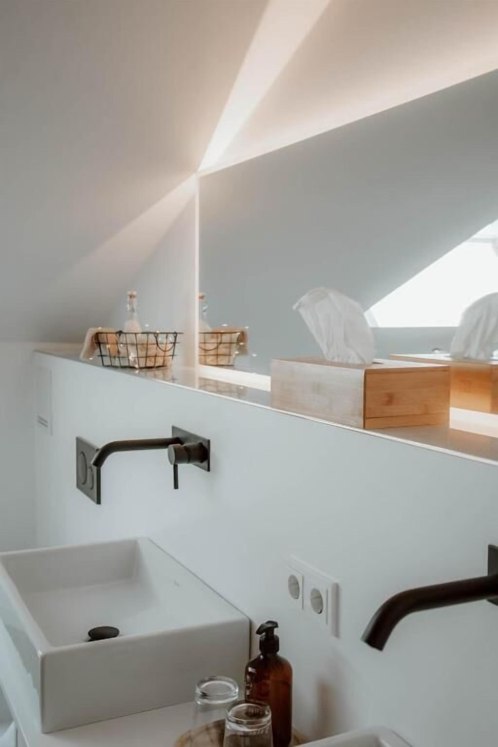 Une salle de bain moderne avec un lavabo blanc, un meuble-lavabo en bois, un miroir et une fenêtre laissant entrer la lumière naturelle.