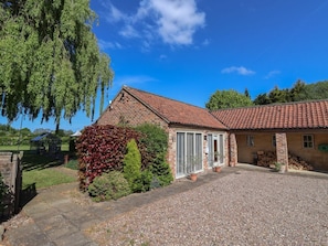 A brick house with a red-tiled roof, a gravel driveway, and a garden with various plants.