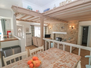 A cozy living area with a dining table, a kitchen, and a stone fireplace. - Claire Cottage, Swanage (Swanage)