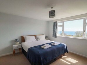 Um quarto com cama, mesa de cabeceira, abajur, janela com vista e cortina.