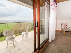 Un balcón con dos sillas blancas, una puerta de cristal y vistas a un campo verde.