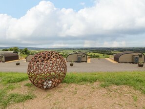 Una escultura metálica esférica en un campo cubierto de hierba, con alojamientos tipo caravana al fondo.