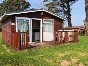 A small, single-story cabin with a sliding glass door entrance, a small kitchen area visible through the door, and a fenced deck area.