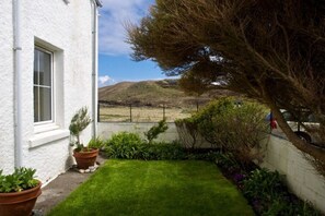 A white building with a window, a grassy lawn, and a view of a hill.
