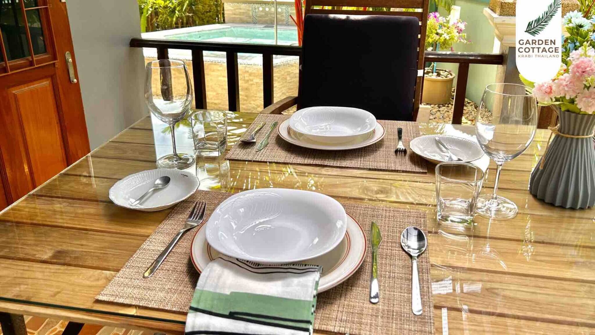 A dining table set for two with plates, cutlery, and glasses, a chair, and a view of the outdoors.