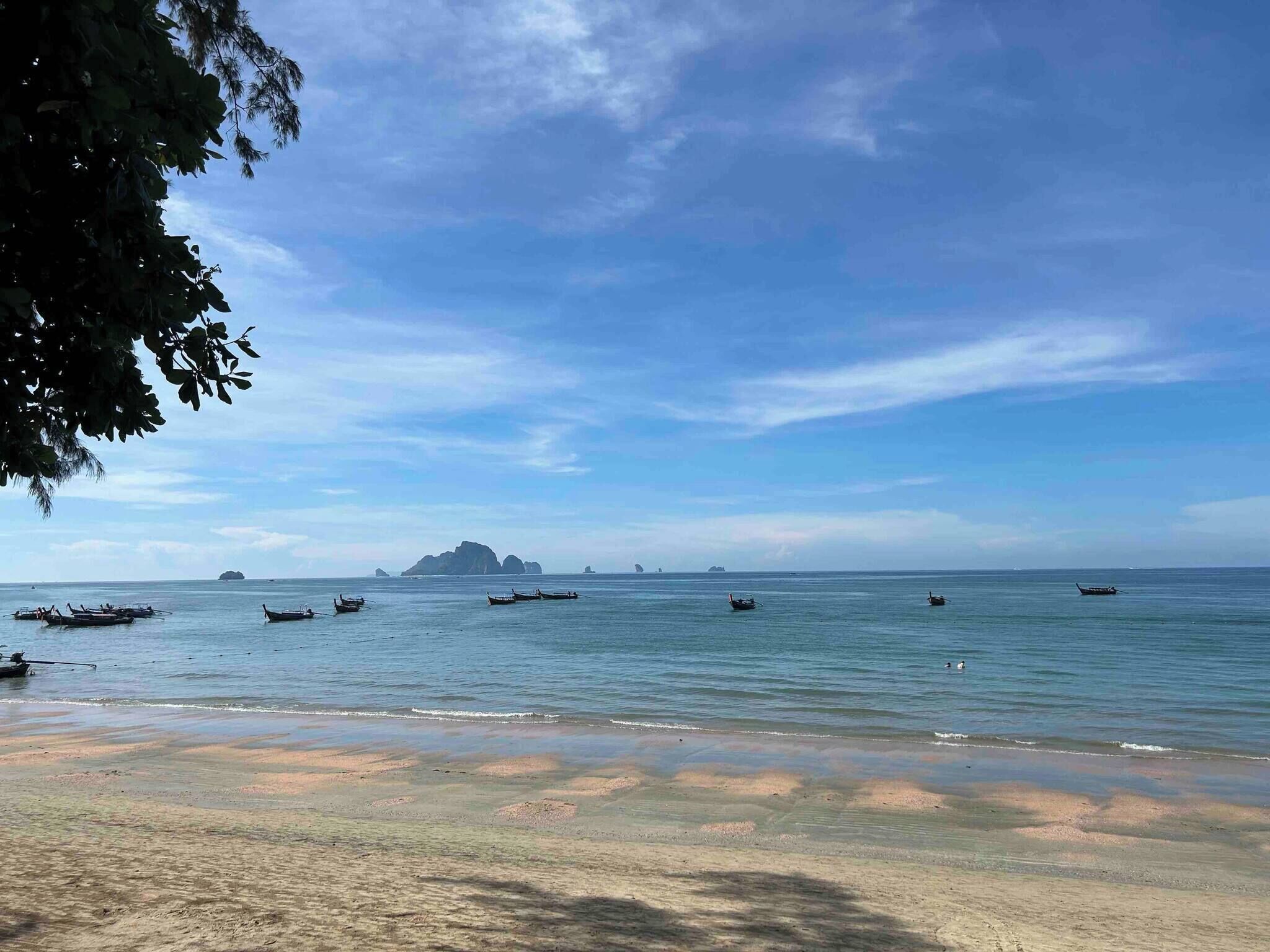 Una playa con barcos, agua cristalina y islas a lo lejos.