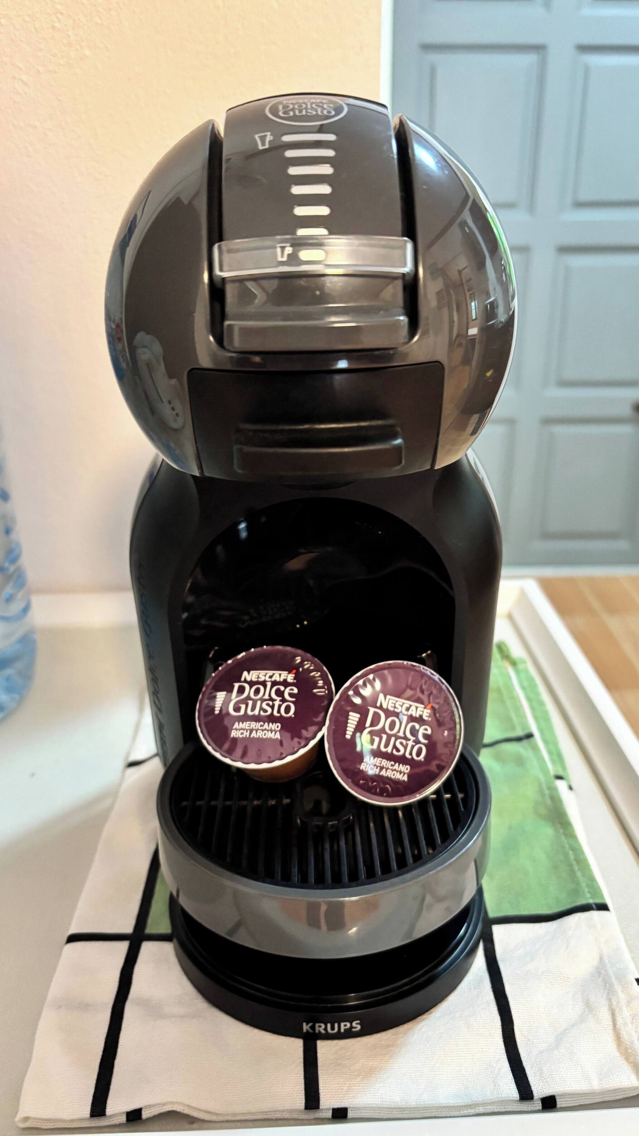 A coffee maker with two Nescafe Dolce Gusto pods on a kitchen counter.