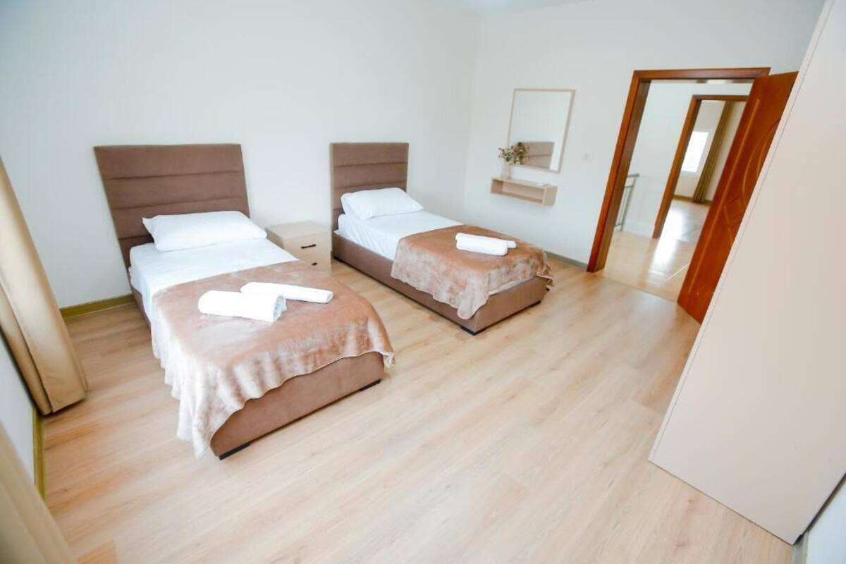 A hotel room with two beds, a wooden floor, a mirror, and a small plant.