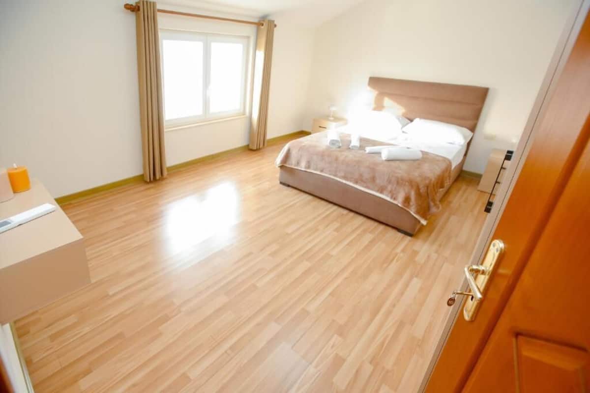 A hotel room with a bed, bedside table, and a window with curtains.