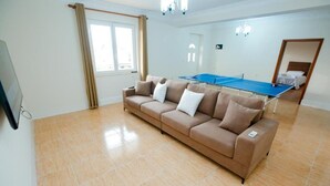 Ein Wohnzimmer mit einer Couch, einem Tischtennisschrank, einem Fernseher und einem Fenster mit Vorhängen.