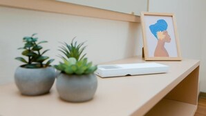 Ein Schreibtisch mit zwei Blumentöpfen, einem gerahmten Kunstwerk und einem weißen elektronischen Gerät.