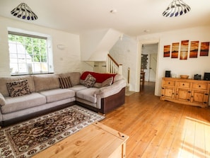 A living room with a sofa, a wooden coffee table, a patterned rug, a staircase, and a wooden cabinet.