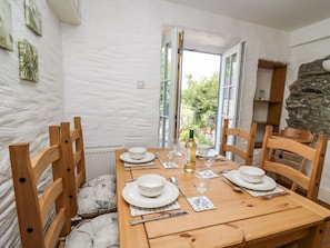 A dining room with a wooden table set for four, chairs, a stone wall, and a view through open doors.