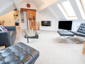 A spacious loft with a high ceiling, a glass coffee table, leather sofas, and a TV mounted on the wall.