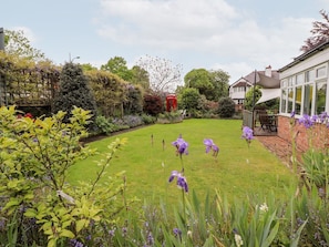 A garden with a lawn, purple flowers, and a red telephone booth.
