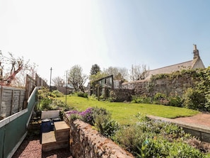 A stone wall, a grassy garden, and a building with a chimney.