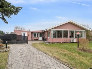 A single-story house with a paved driveway, a black fence, and a lawn.