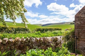 A stone wall, lush greenery, and a stone building. - Old Smiddy Cottage, Haddington (Dunbar)