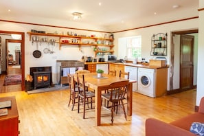 A cozy kitchen with wooden furniture, a stove, and a washing machine. - Old Smiddy Cottage, Haddington (Dunbar)