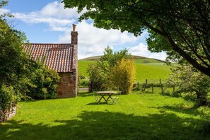 A brick building with a tiled roof, surrounded by lush green grass and trees. - Old Smiddy Cottage, Haddington (Dunbar)