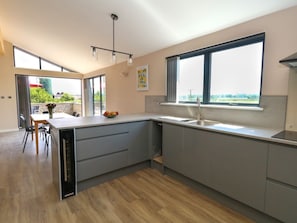Una cocina moderna con una isla grande, un comedor con sillas y vistas amplias a través de ventanas grandes.