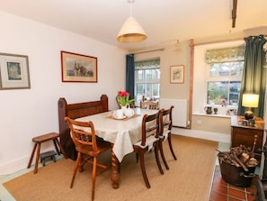 A dining area with a wooden table, chairs, a hanging light fixture, framed artwork on the walls, and a window with curtains. - IVY COTTAGE, WiFi, Woodburner, Snug room, Buxton (Buxton)