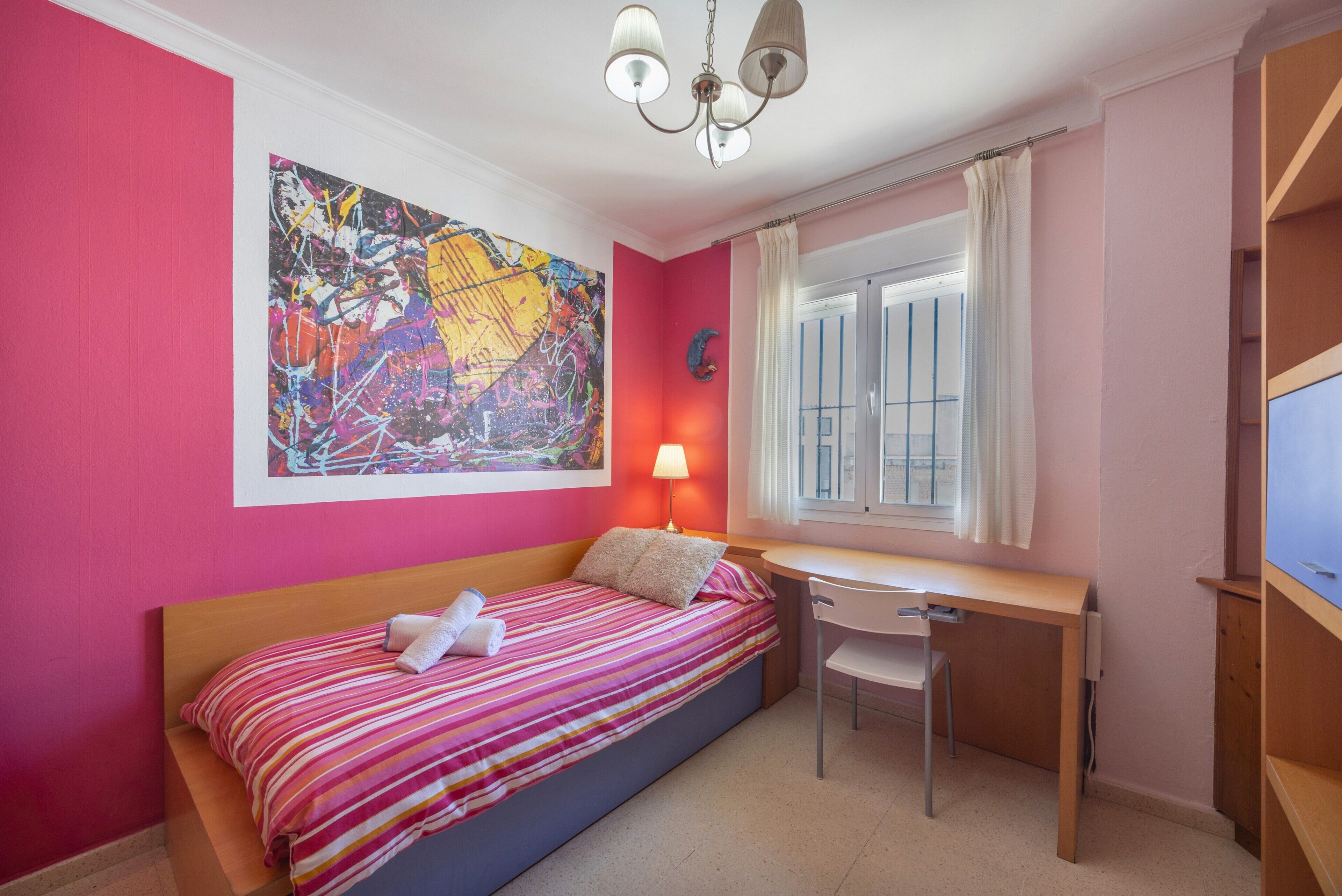 Un dormitorio con cama, escritorio, silla y un cuadro abstracto grande en la pared.