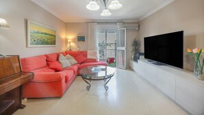 Een woonkamer met een rode bank, een glazen salontafel, een televisie en een balkon met uitzicht.