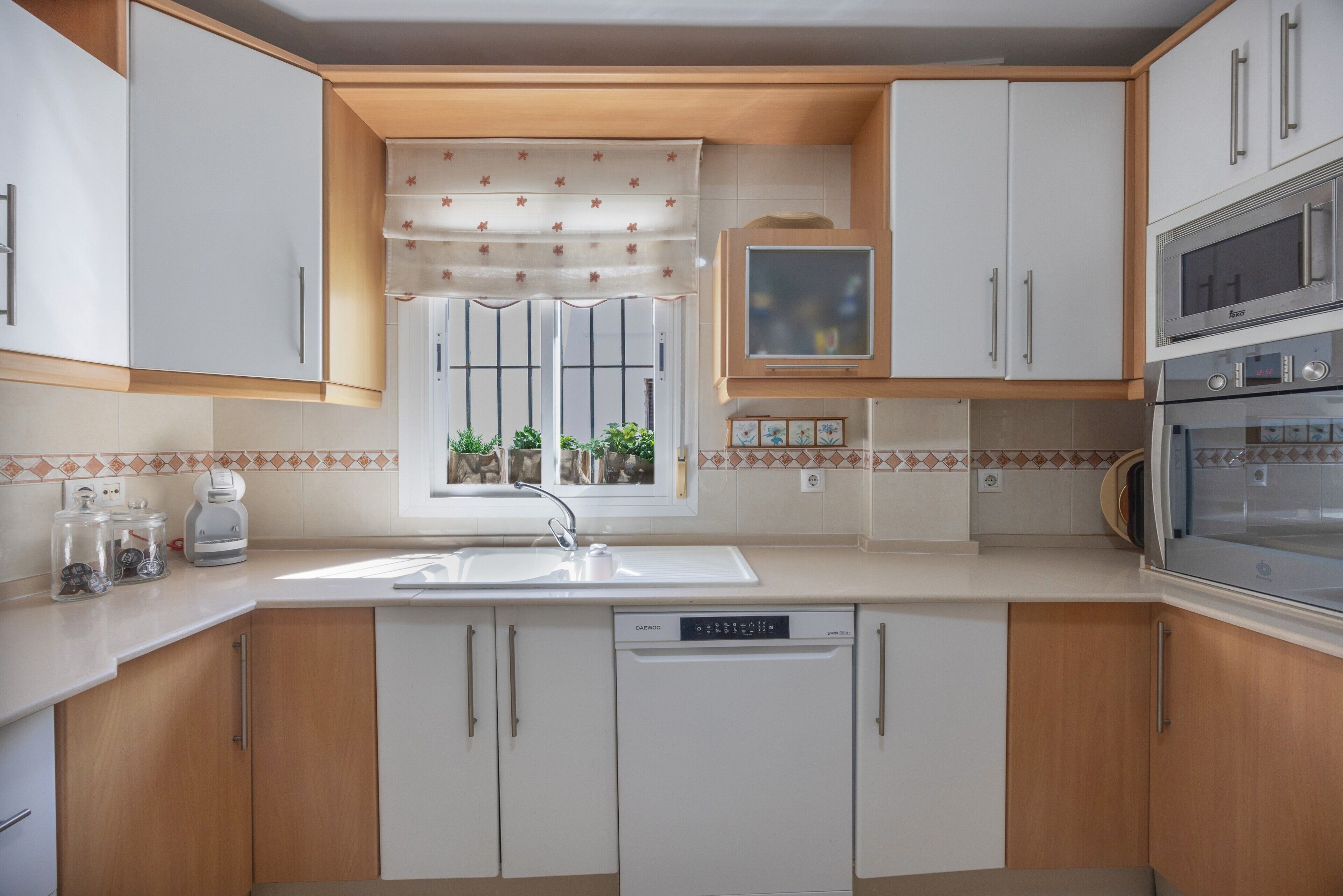 Una cocina moderna con armarios blancos, lavavajillas empotrado, microondas y ventana con vistas al exterior.