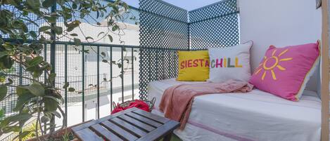 Un balcón con una cama, una mesa y una planta.