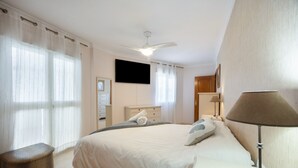 Een slaapkamer met een bed, nachtkastje, lamp, plafondventilator en een televisie.