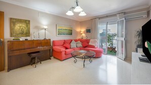 Een woonkamer met een rode bank, een glazen salontafel, een houten bureau en een schilderij aan de wand.