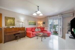 Ein Wohnzimmer mit einem roten Sofa, einem Glastisch, einem Holzbüro und einem Bild an der Wand.