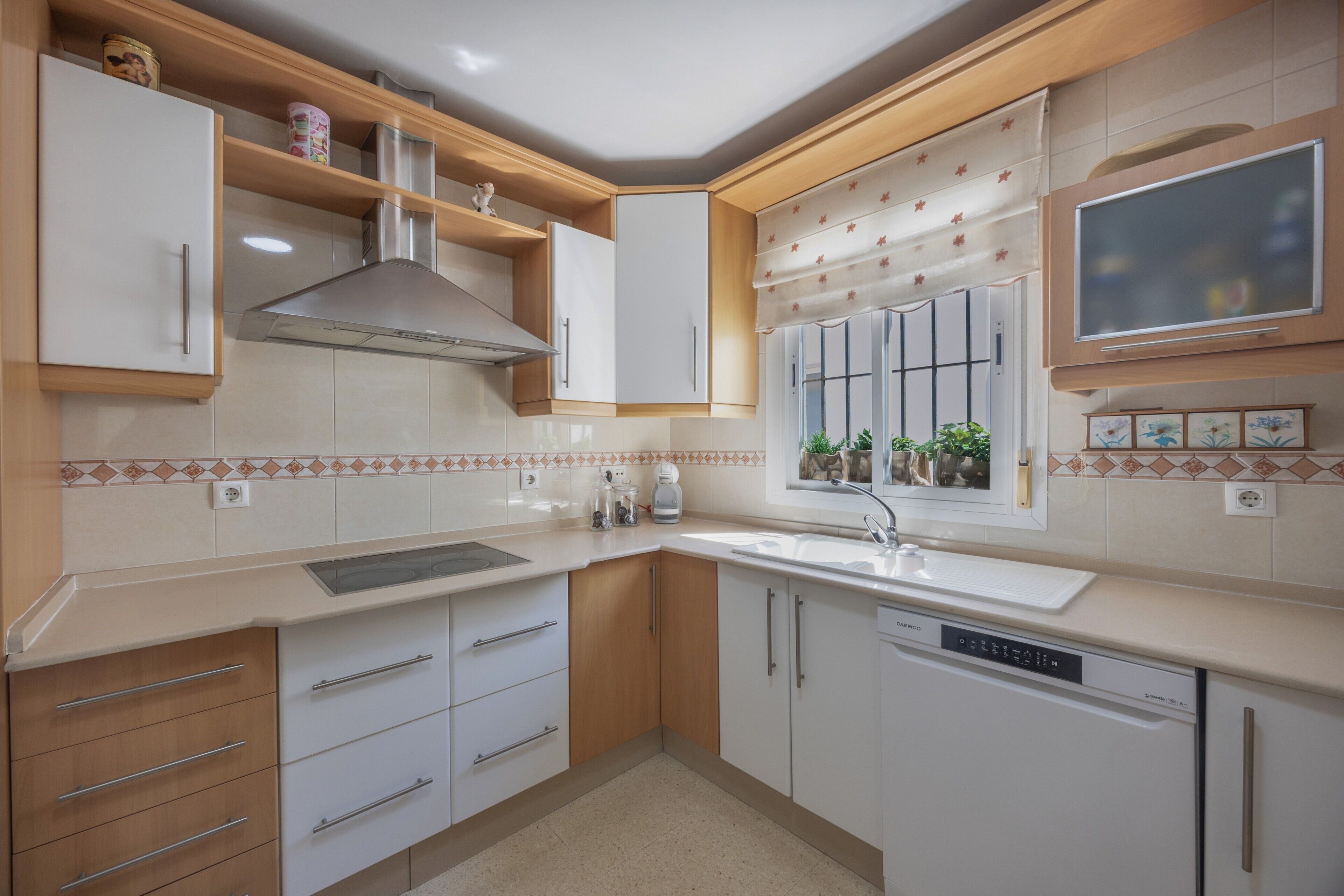 Una cocina moderna con armarios blancos, lavavajillas, estufa y una ventana con plantas.