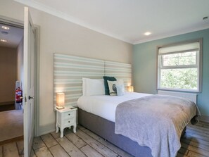 A bedroom with a bed, bedside tables, a window, and a door. - Saxon Lodge Cottage, Felixstowe, Suffolk (Felixstowe)