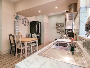 A kitchen with a marble countertop, a stainless steel sink, a black refrigerator, and a wall clock. - Saxon Lodge Cottage, Felixstowe, Suffolk (Felixstowe)