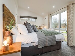 A bedroom with a bed, bedside table, lamp, window, and curtains.