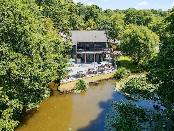 A two-story building with a balcony, surrounded by lush greenery and a small water body.