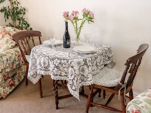A round table with a lace tablecloth, two chairs, a vase with pink flowers, a bottle, and two glasses. - Marsh Cottage, is in Oxenhope. (Keighley)