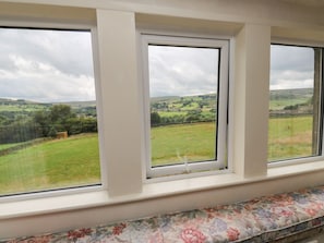 A window with a view of a green field and distant hills. - Marsh Cottage, is in Oxenhope. (Keighley)